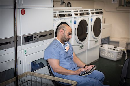 Mature man in surgical scrubs using touchscreen on digital tablet in laundry room Stock Photo - Premium Royalty-Free, Code: 614-08000372