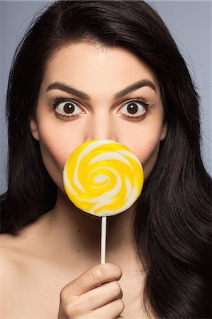 portrait in front of grey background - Mid adult woman holding yellow lollipop in front of face Stock Photo - Premium Royalty-Free, Code: 614-08030691