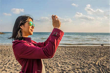 Mid adult woman on beach taking photo Stock Photo - Premium Royalty-Free, Code: 614-08030742