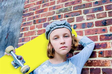 Portrait of sullen tomboy skateboarder girl leaning against brick wall Fotografie stock - Premium Royalty-Free, Codice: 614-08030978