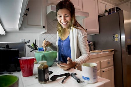 Woman preparing food in kitchen whilst reading recipe from smartphone Photographie de stock - Premium Libres de Droits, Code: 614-08030972