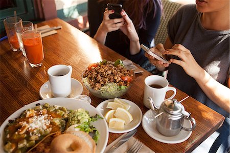 Cropped shot of  female friends texting on smartphones in vegetarian restaurant Photographie de stock - Premium Libres de Droits, Code: 614-08031004