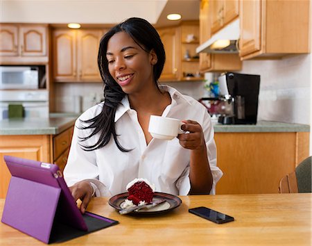 Young woman using digital tablet at kitchen table Stock Photo - Premium Royalty-Free, Code: 614-08065971
