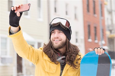 Smiling male snowboarder taking smartphone selfie in street Stock Photo - Premium Royalty-Free, Code: 614-08066024