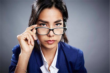 portrait of confident businesswoman studio - Portrait of young woman looking over eyeglasses Stock Photo - Premium Royalty-Free, Code: 614-08066052