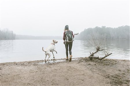 Young woman throwing stick for her dog on misty lakeside Stock Photo - Premium Royalty-Free, Code: 614-08081226