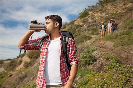 Young man at bottom of hill, drinking from flask, friends trailing behind Stock Photo - Premium Royalty-Free, Code: 614-08081289