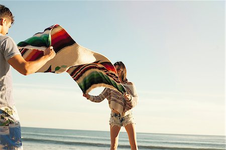 Young couple at beach, shaking out picnic blanket Stock Photo - Premium Royalty-Free, Code: 614-08081310