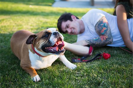 Young man lying in park petting bulldog Foto de stock - Royalty Free Premium, Número: 614-08119483