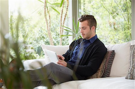 Man relaxing on sofa with feet up looking at digital tablet Stock Photo - Premium Royalty-Free, Code: 614-08119687