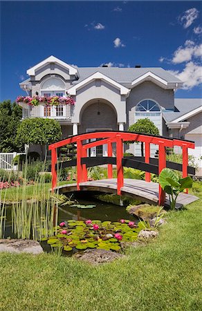 simsearch:614-08119682,k - Grey brick cottage style residential home and landscaped  manicured garden with red wooden footbridge, Quebec, Canada Photographie de stock - Premium Libres de Droits, Code: 614-08119683