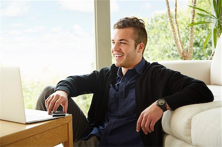 Portrait of smiling man sitting on floor holding smartphone Stock Photo - Premium Royalty-Free, Code: 614-08119694