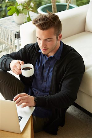 Portrait of man sitting on floor at home looking at laptop and drinking cup of coffee Foto de stock - Sin royalties Premium, Código: 614-08119691