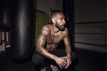 Tattooed male boxer crouching next to punch bag in gym Photographie de stock - Premium Libres de Droits, Code: 614-08119878