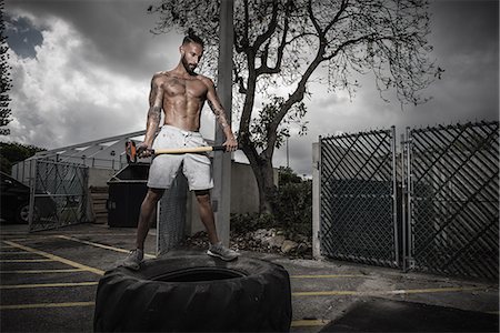 Poised male boxer standing on truck tyre holding sledge hammer in yard Photographie de stock - Premium Libres de Droits, Code: 614-08119888