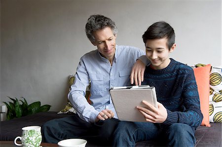 sweaters - Father and teenage son reading digital tablet on sofa Stock Photo - Premium Royalty-Free, Code: 614-08126746