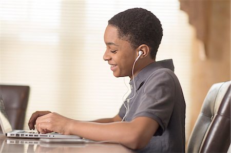 Teenage boy at dining table typing on laptop Stock Photo - Premium Royalty-Free, Code: 614-08126777