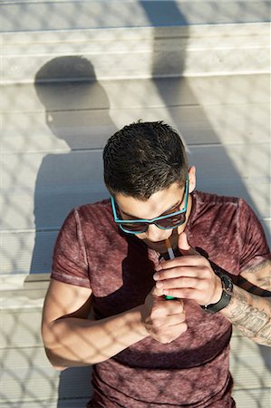 High angle view of young man lighting cigarette on park bench Stock Photo - Premium Royalty-Free, Code: 614-08126770