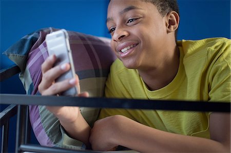 Close up of teenage boy lying in bunkbed reading smartphone text Stock Photo - Premium Royalty-Free, Code: 614-08126787