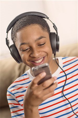 Teenage boy wearing headphones reading smartphone texts Stock Photo - Premium Royalty-Free, Code: 614-08126782