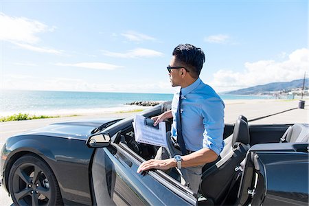 Young businessman getting out of car at coastal parking lot with paperwork Stock Photo - Premium Royalty-Free, Code: 614-08126818