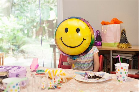 simsearch:614-08120078,k - Girl sitting at birthday party table with cake playing with smiley face balloon Stock Photo - Premium Royalty-Free, Code: 614-08120078