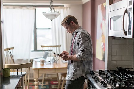 pantalla táctil - Mid adult man in kitchen using touchscreen on digital tablet Foto de stock - Sin royalties Premium, Código: 614-08148575