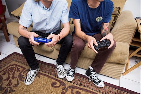 Two young men sitting on sofa, playing video game, low section Foto de stock - Sin royalties Premium, Código: 614-08148645