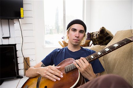 simsearch:614-09253850,k - Young man sitting on sofa, playing guitar Foto de stock - Sin royalties Premium, Código: 614-08148646