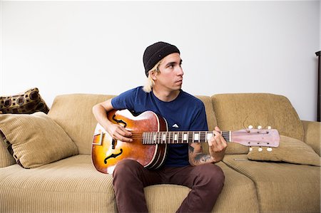 simsearch:614-09253850,k - Young man sitting on sofa, playing guitar Stockbilder - Premium RF Lizenzfrei, Bildnummer: 614-08148647