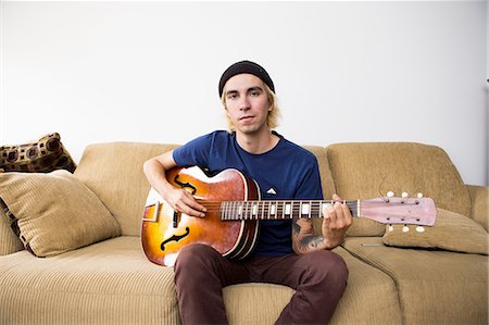 simsearch:614-09253850,k - Young man sitting on sofa, playing guitar Stockbilder - Premium RF Lizenzfrei, Bildnummer: 614-08148648