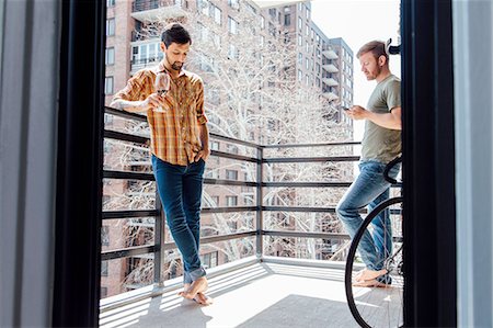 simsearch:614-08392622,k - Male couple standing on balcony, standing away from each  other, drinking wine and looking at smartphone Stock Photo - Premium Royalty-Free, Code: 614-08148687