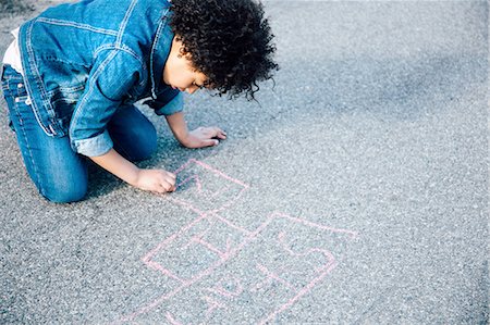 High angle view of girl kneeling using chalk to draw hopscotch game Fotografie stock - Premium Royalty-Free, Codice: 614-08201868