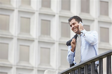 Mid adult business man with jacket over shoulder using smartphone to make telephone call, smiling Stock Photo - Premium Royalty-Free, Code: 614-08201937