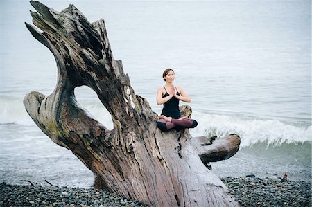 simsearch:614-09135006,k - Mature woman practicing yoga lotus position on large driftwood tree trunk at beach Fotografie stock - Premium Royalty-Free, Codice: 614-08201985