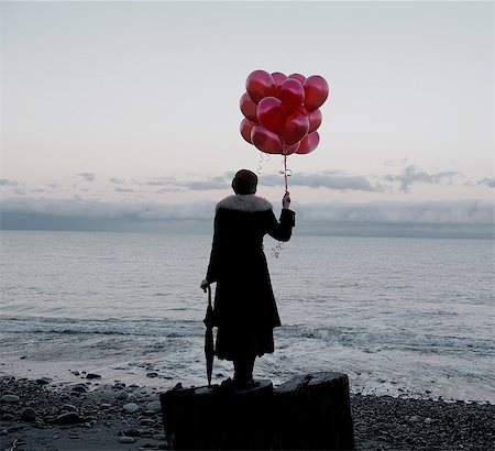 retro fashion for women - Woman holding bunch of red balloons standing large driftwood tree stump on beach Stock Photo - Premium Royalty-Free, Code: 614-08201987