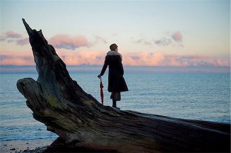 simsearch:614-08383692,k - Woman leaning on umbrella standing on large driftwood tree trunk on beach Foto de stock - Sin royalties Premium, Código: 614-08201988