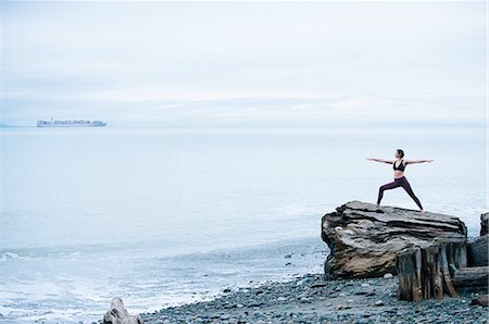 Mature woman practicing yoga pose whilst standing on large driftwood tree stump on beach Foto de stock - Sin royalties Premium, Código: 614-08201981