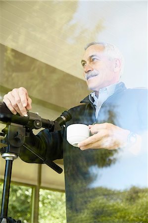 person focusing telescope - Senior man at home, drinking coffee, using telescope through window Stock Photo - Premium Royalty-Free, Code: 614-08202033