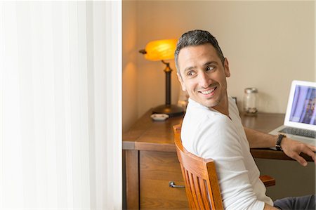 Mid adult man sitting at desk, using laptop Stock Photo - Premium Royalty-Free, Code: 614-08202063