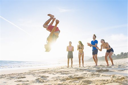 Group of friends on beach watching friend do somersault Foto de stock - Royalty Free Premium, Número: 614-08202263