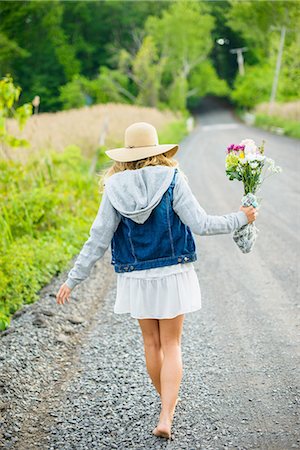 Rear view of bare footed young woman walking on rural gravel road carrying bunch of flowers Stock Photo - Premium Royalty-Free, Code: 614-08202316