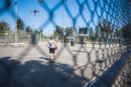 simsearch:649-07520889,k - Young male basketball player behind court fence looking at basketball hoop Fotografie stock - Premium Royalty-Free, Codice: 614-08202335