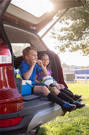 sports park - Boy and younger sister sitting in car boot eating oranges on football practice break Stock Photo - Premium Royalty-Free, Code: 614-08219836