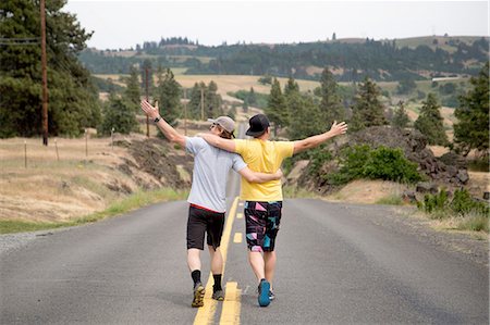 Two men walking along road together, arms raised, appreciating view, rear view Stock Photo - Premium Royalty-Free, Code: 614-08219870