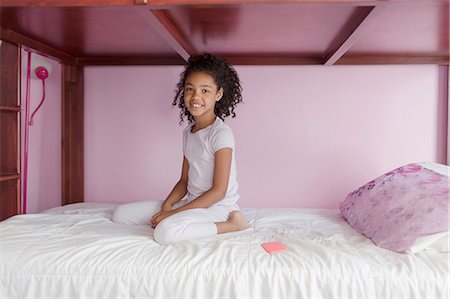 Girl wearing pyjamas kneeling on bed, looking at camera smiling Fotografie stock - Premium Royalty-Free, Codice: 614-08219923