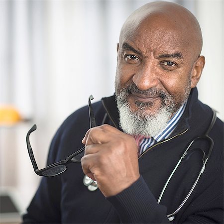 Portrait of mature doctor with stethescope, holding glasses, looking at camera smiling Stock Photo - Premium Royalty-Free, Code: 614-08219945