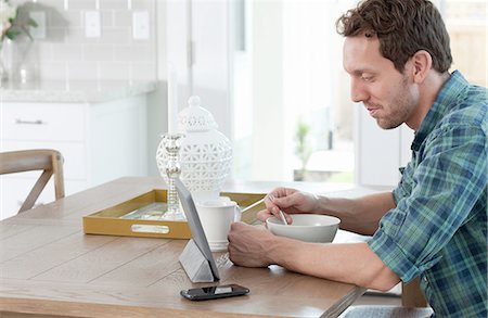 skype - Mid adult man eating breakfast, whilst looking at digital tablet Foto de stock - Sin royalties Premium, Código: 614-08219958