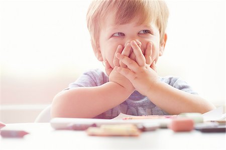 Boy sitting at table resting on elbows, covering mouth with hands, looking away Stock Photo - Premium Royalty-Free, Code: 614-08220011