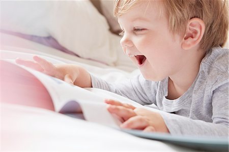 schlafenszeit - Head and shoulders of boy on bed lying on front looking at storybook, laughing Stockbilder - Premium RF Lizenzfrei, Bildnummer: 614-08220020